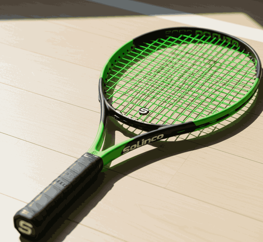 Green and black Solinco tennis racquet with matching strings on a light wood floor in sunlight